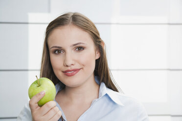 Germany, Cologne, Young woman with green apple, smiling, portrait - PDF000106