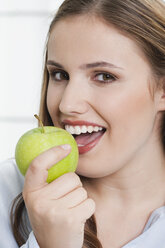 Germany, Cologne, Young woman with green apple, smiling, portrait - PDF000108