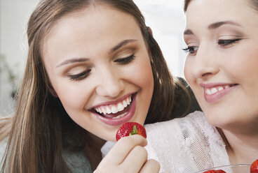 Deutschland, Köln, Junge Frauen essen Erdbeere, lächelnd - PDF000155