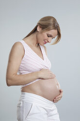 Schwangere Frau im mittleren Erwachsenenalter beobachtet ihren Bauch - RBF000443