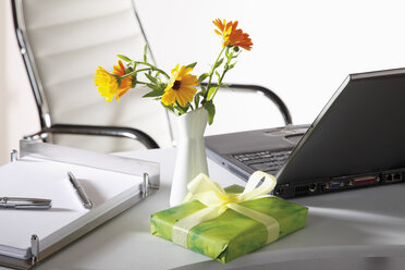 Office scene with flower vase, gift parcel and laptop on desktop - CSF014058