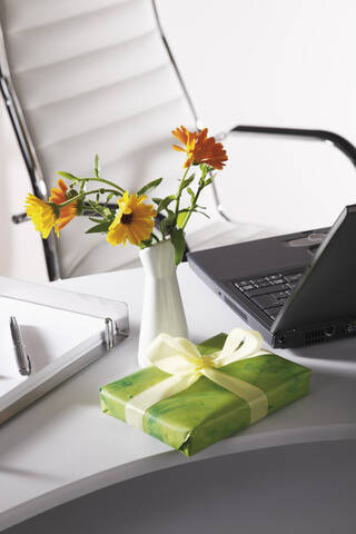 Büroszene mit Blumenvase, Geschenkpaket und Laptop auf dem Schreibtisch, lizenzfreies Stockfoto