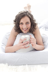Deutschland, Leipzig, Junge Frau auf Bett liegend mit Kaffeetasse, lächelnd, Porträt - MBF001215
