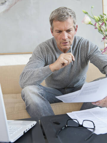 Germany, Munich, Mature man doing paperwork with laptop stock photo
