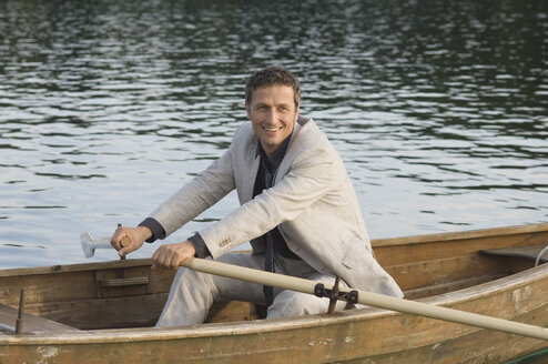 Germany, Bavaria, Wesslinger See, Business man rowing boat in lake after work - CRF002011