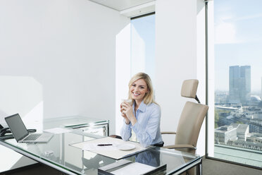 Deutschland, Frankfurt, Geschäftsfrau sitzend im Büro mit Kaffeetasse - SKF000432