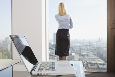 Deutschland, Frankfurt, Geschäftsfrau schaut durch ein Fenster mit Laptop im Vordergrund - SKF000445