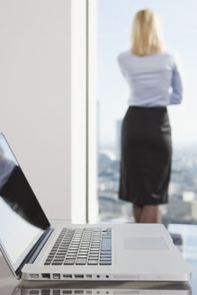 Deutschland, Frankfurt, Geschäftsfrau schaut durch ein Fenster mit Laptop im Vordergrund - SKF000446