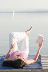 Mittlere erwachsene Frau liegt auf einem Steg und liest ein Buch - UMF000332