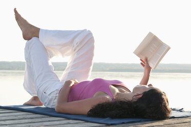 Mittlere erwachsene Frau liegt auf einem Steg und liest ein Buch - UMF000333