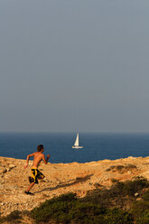 Portugal, Algarve, Sagres,Junger Mann läuft am Strand von Tonel, Segelboot im Hintergrund - WVF000155