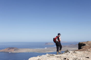 Spanien, Kanarische Inseln, Lanzarote, Risco de Famara, Ältere Frau geht auf Klippe, Insel La Graciosa im Hintergrund - SIEF000505