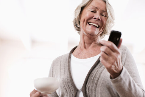 Deutschland, Wakendorf, Ältere Frau benutzt Handy und lächelt - WESTF016201