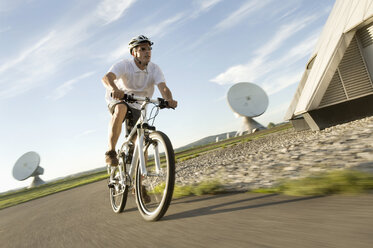 Deutschland, Bayern, Raisting, Älterer Mann fährt Fahrrad in der Nähe eines Radiosenders - RNF000654