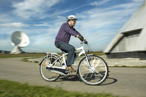 Germany, Bavaria, Raisting, Man riding electric bicycle near radio station - RNF000657