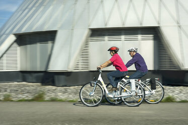 Germany, Bavaria, Raisting, Senior couple riding electric bicycle near radio station - RNF000658