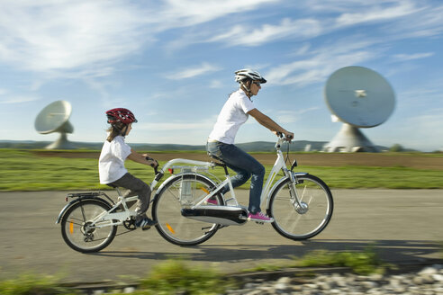 Germany, Bavaria, Raisting, Woman with girl riding electric bicycle near radio station - RNF000660