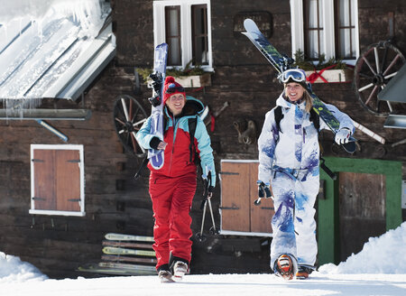 Österreich, Kleinwalsertal, Frauen tragen Ski auf den Schultern bei einer Berghütte - MRF001239
