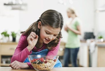 Germany, Cologne, Girl looking at muesli in bowl, mother in background - WESTF016295