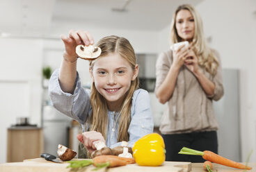 Germany, Cologne, Daughter cutting vegetable with mother in background - WESTF016318