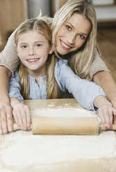 Germany, Cologne, Mother and daughter rolling dough, smiling, portrait - WESTF016321