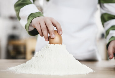 Germany, Cologne, Boy putting egg on heap of flour - WESTF016335