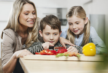 Germany, Cologne, Mother and children cutting vegetables in kitchen - WESTF016350