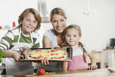 Germany, Cologne, Mother and children making pizza in kitchen - WESTF016365