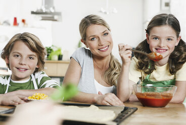 Germany, Cologne, Mother and children making pizza in kitchen - WESTF016366