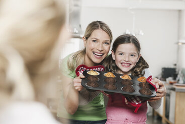 Deutschland, Köln, Mutter und Tochter halten Tassenkuchen in einem Backblech, lächelnd - WESTF016371