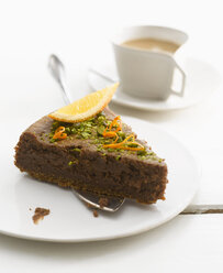 Plate of brownie cake garnished with orange slice and pistachios, close-up - KSWF000680