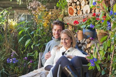 Österreich, Salzburg, Flachau, Mann und Frau auf Bank im Garten eines Bauernhofs sitzend, lächelnd, Porträt - HHF003522