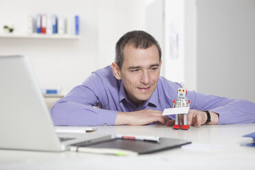 Germany, Bavaria, Munich, Businessman in office playing with roboter - RBF000474