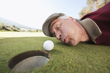 Italy, Kastelruth, Mature man blowing golf ball into hole - WESTF016411