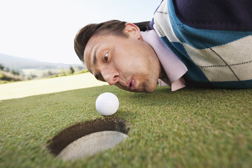 Italien, Kastelruth, Mittlerer Erwachsener, der einen Golfball in ein Loch schlägt - WESTF016440