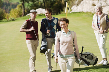 Italien, Kastelruth, Mittlere erwachsene Frau lächelnd mit Golfspielern im Hintergrund auf Golfplatz - WESTF016559