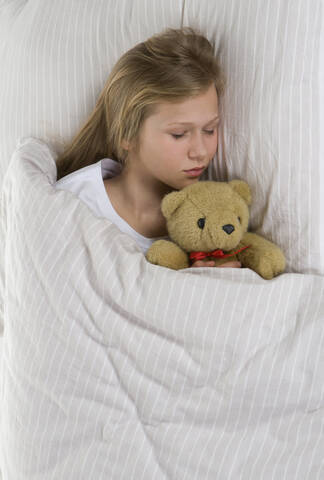 Girl sleeping on bed with teddy bear stock photo