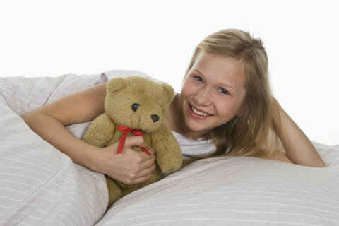 Girl lying on bed with teddy bear, smiling stock photo