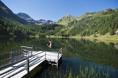 Austria, Styria, Mid adult woman jumping into lake duisitzkar in schladming - HHF003541