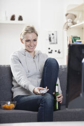 Deutschland, München, Junge Frau sieht fern, lächelnd - RBF000531