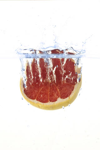 In Wasser fallende Grapefruit vor weißem Hintergrund, lizenzfreies Stockfoto
