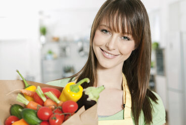 Germany, Cologne, Woman standing in kitchen with vegetables bag - FMKF000189