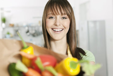 Germany, Cologne, Woman standing in kitchen with vegetables bag - FMKF000190