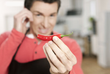 Germany, Cologne, Man holding red chilli - FMKF000214