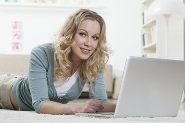 Germany, Bavaria, Munich, Woman lying on floor and using laptop, portrait - RBF000538