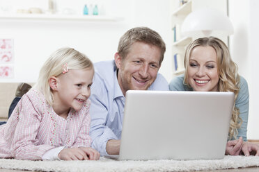 Germany, Bavaria, Munich, Family lying on carpet and using laptop, smiling - RBF000553