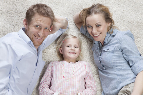 Deutschland, Bayern, München, Eltern mit Tochter auf Teppich liegend, lächelnd, Porträt - RBF000562