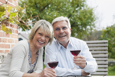 Germany, Kratzeburg, Senior couple with wine glass sitting near country house - WESTF016696