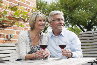 Germany, Kratzeburg, Senior couple with wine glass sitting near country house - WESTF016697