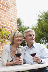 Germany, Kratzeburg, Senior couple with wine glass sitting near country house - WESTF016698